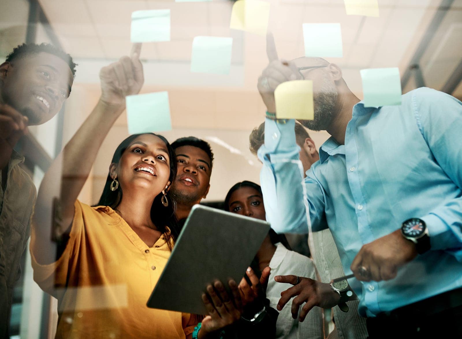 62806880_business-team-and-tablet-with-sticky-notes-on-glass-wall-for-brainstorming-project-ideas-or-kpi-review-in-office-happy-people-collaboration-and-pointing-to-paper-for-progress-report-or-development