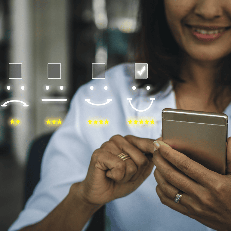 A close-up of a smiling woman in a white top using a smartphone, with a transparent overlay of a customer satisfaction survey. The overlay shows a row of faces from sad to happy with star ratings beneath, and a checked box above the happiest face indicating a five-star rating. The background is an indoor setting with a blurred, bokeh effect.